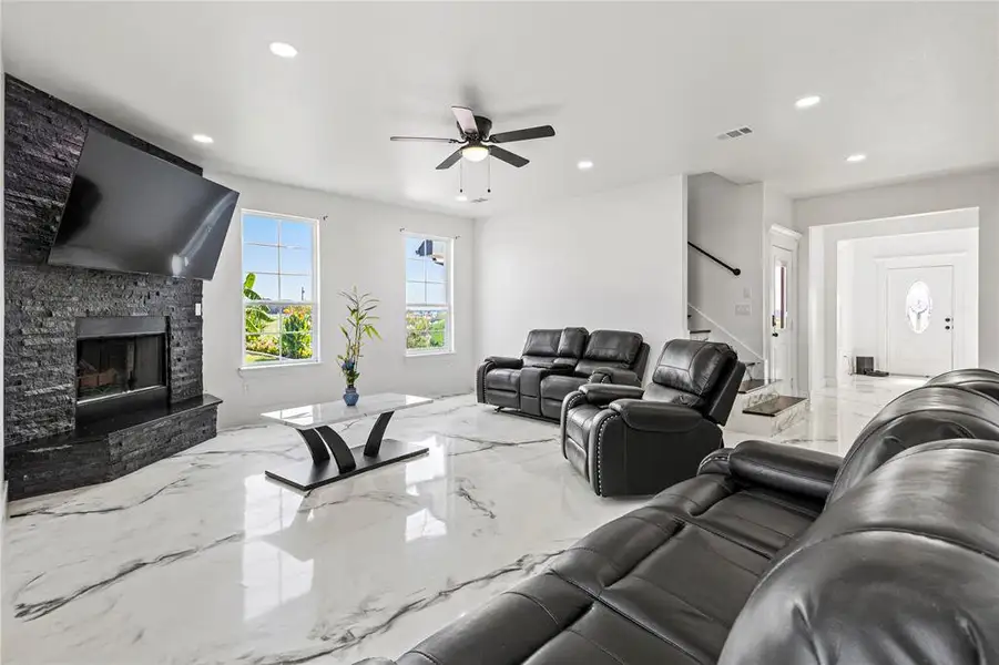 Living area featuring light marble finish flooring, recessed lighting, a fireplace, a ceiling fan, and stairs Living area featuring light marble finish flooring, recessed lighting, a fireplace, a ceiling fan, and stairs