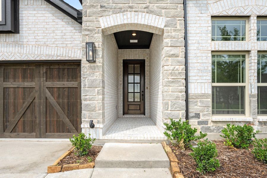 Home entrance with stone arch, dark wood front door, and rustic garage door on white brick exterior Home entrance with stone arch, dark wood front door, and rustic garage door on white brick exterior