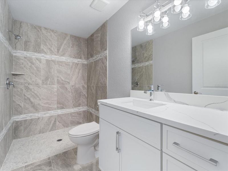Primary's bathroom with fully tiled shower, solid wood cabinetry, and quartz countertop.