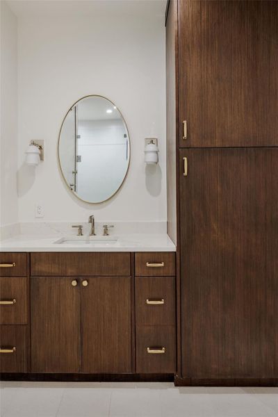 Organic warmth meets modern refinement in this guest bath, where custom walnut cabinetry, brass hardware, and a sculptural oval mirror create a timeless, tailored aesthetic. Organic warmth meets modern refinement in this guest bath, where custom walnut cabinetry, brass hardware, and a sculptural oval mirror create a timeless, tailored aesthetic.