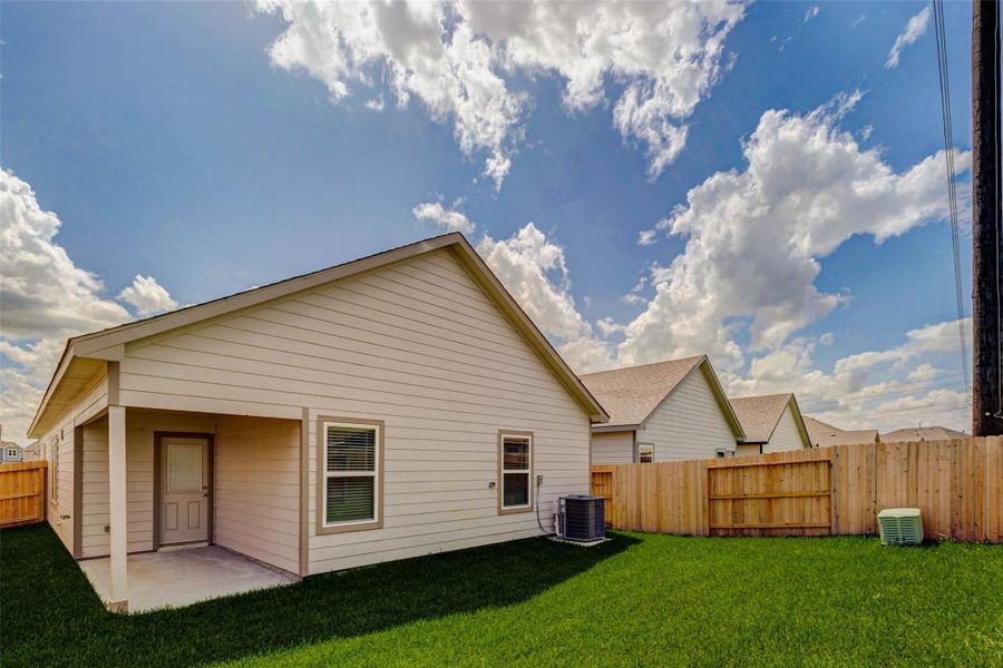 Wide backyard view featuring a covered patio, rear door, private wood fencing, fresh lawn, and open sky. The yard offers a comfortable outdoor area for grilling, seating, gardening, or play, while the covered patio provides shade and a natural spot to enjoy morning coffee or evening relaxation.
