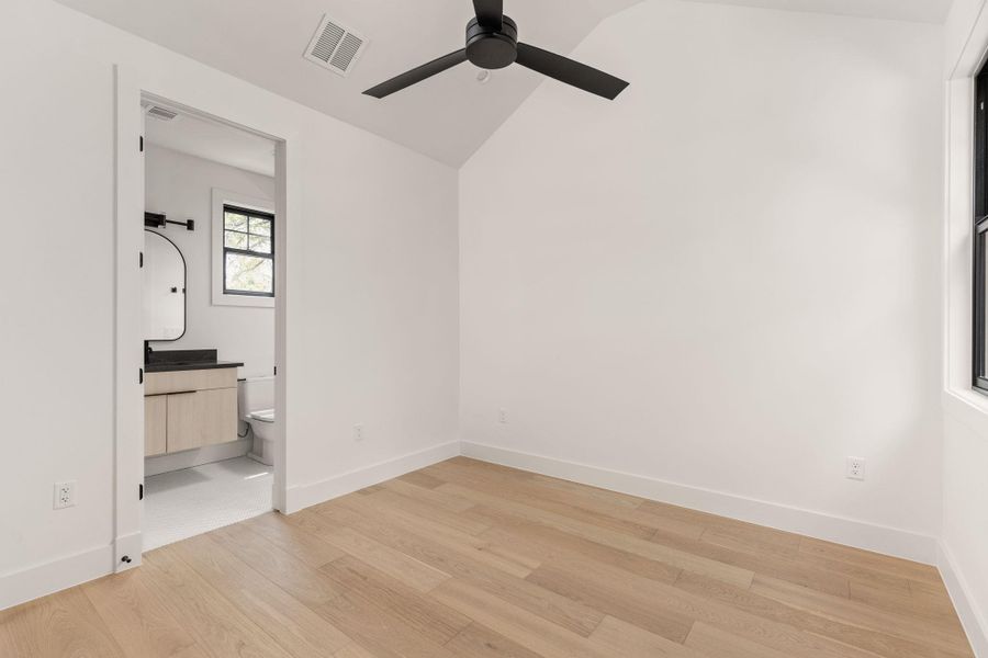 Unfurnished bedroom with lofted ceiling, light wood-type flooring, a ceiling fan, and connected bathroom Unfurnished bedroom with lofted ceiling, light wood-type flooring, a ceiling fan, and connected bathroom