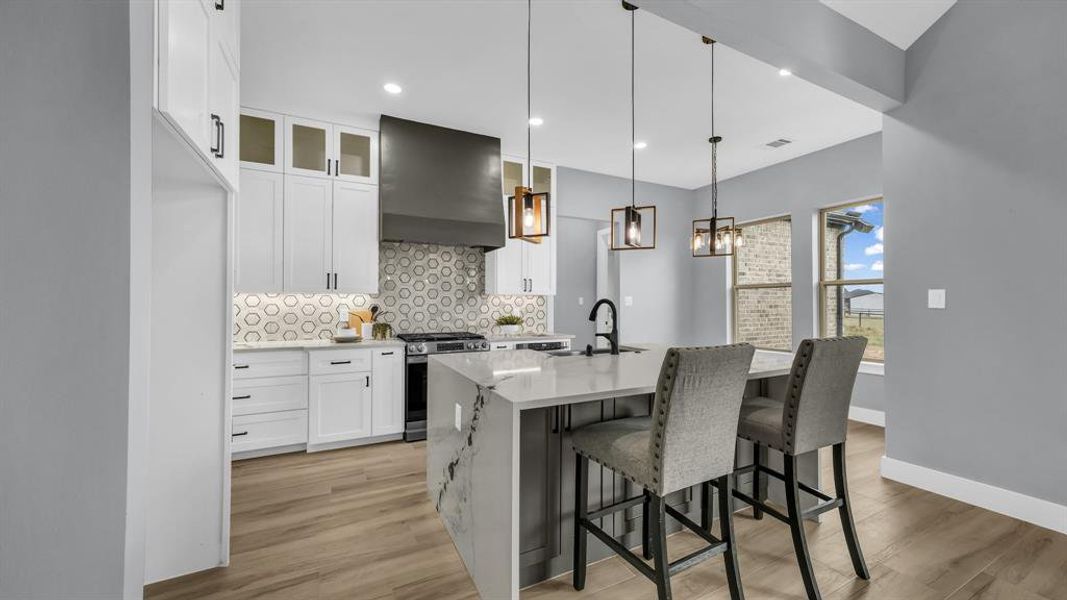 Kitchen featuring white cabinets, a breakfast bar area, pendant lighting, extractor fan, and light stone counters