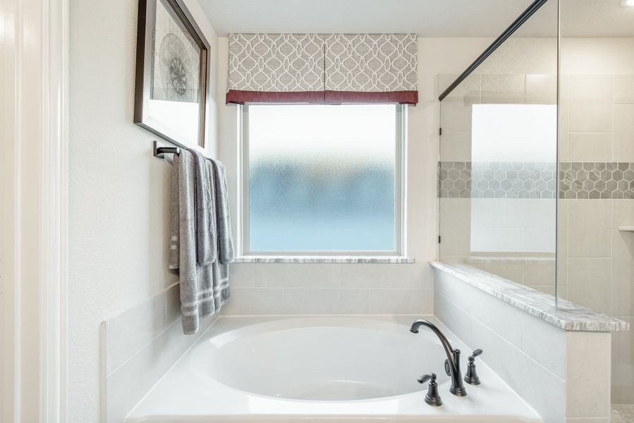 White soaking tub with dark bronze faucet beside a glass-enclosed shower and frosted window in a bright bathroom