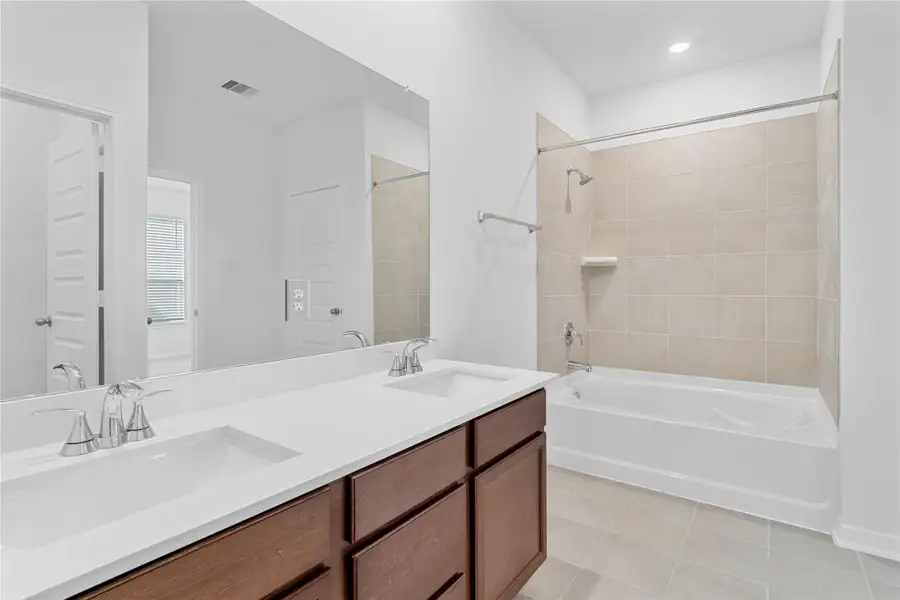 This beautifully updated primary bathroom is move-in ready! It showcases stained cabinetry paired with light countertops, dual vanity sinks, a large mirror, tub/shower combination with tile surround, a spacious walk-in closet with built-in shelving, high ceilings, custom paint, and stylish modern finishes throughout.