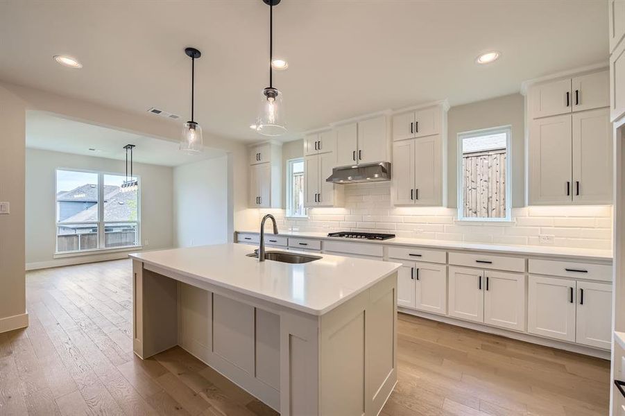 Kitchen featuring under cabinet range hood, light wood-type flooring, tasteful backsplash, gas cooktop, and recessed lighting
