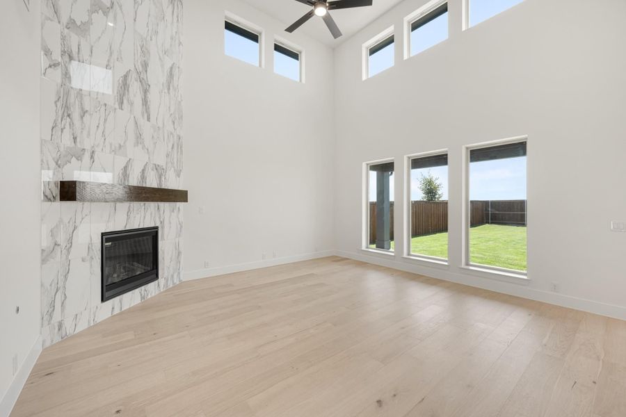 Open living room with marble tile fireplace, high ceilings, ceiling fan, and light hardwood floors