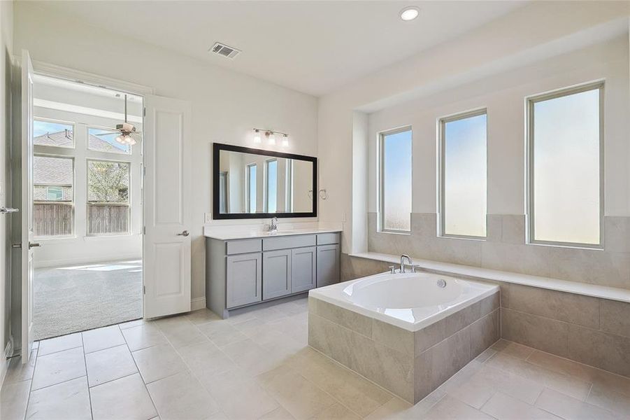 Bathroom with a relaxing tiled tub, ceiling fan, vanity, and tile patterned floors