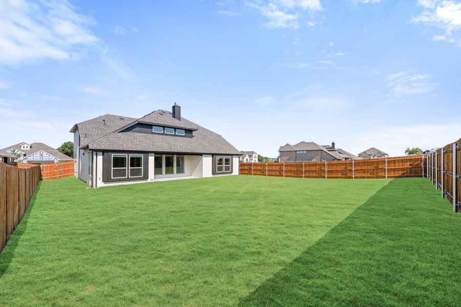 Backyard of a single-story home with large green lawn, wood privacy fence, and gray shingle roof. Backyard of a single-story home with large green lawn, wood privacy fence, and gray shingle roof.