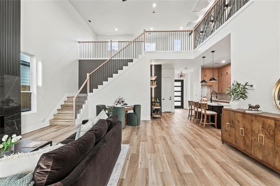 Open concept living area featuring wood-finish flooring, a two-story ceiling, and a prominent staircase with dark metal balusters