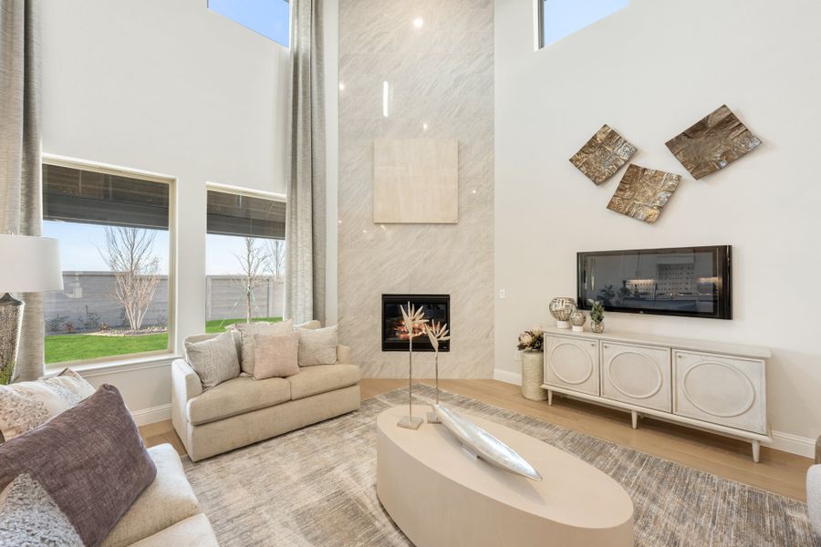 Living room with two-story ceiling, marble fireplace surround, neutral sofas, and wall-mounted TV