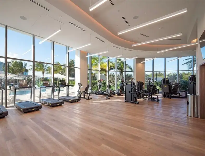 Fitness facility featuring floor-to-ceiling windows, wood-finish flooring, curved architectural ceiling detail, and recessed linear lighting