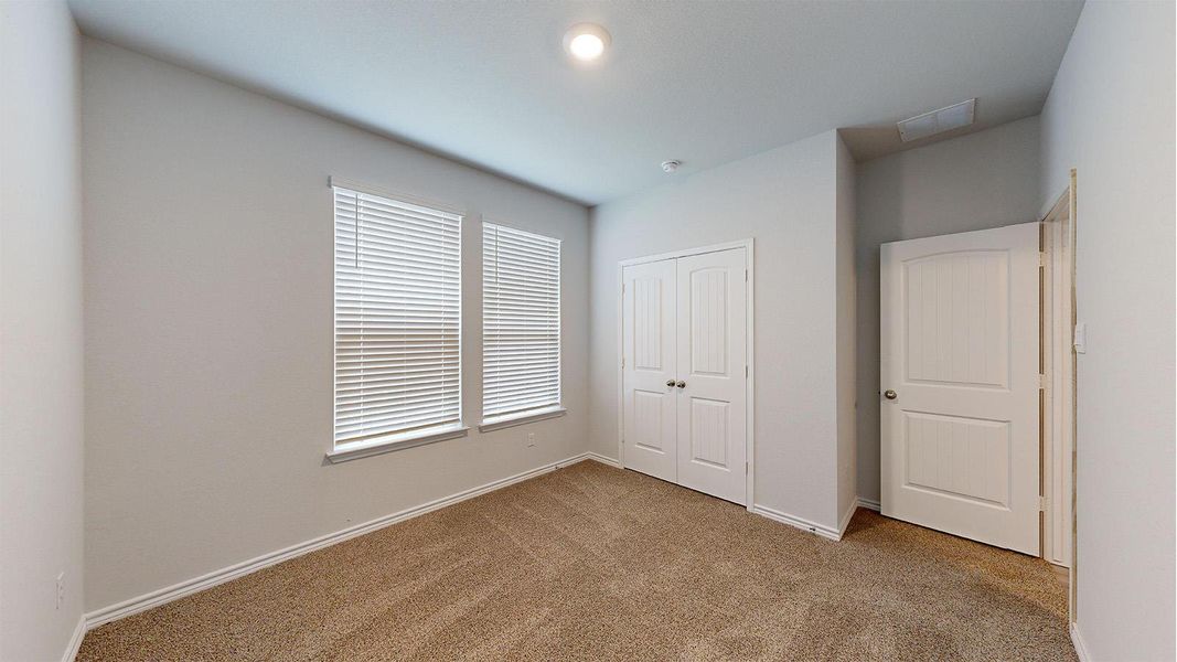 Carpeted room featuring dual windows with horizontal blinds, a bi-fold closet door, and a traditional paneled door Carpeted room featuring dual windows with horizontal blinds, a bi-fold closet door, and a traditional paneled door