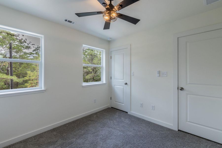 Interior space featuring gray carpet flooring, white walls, two windows, two white paneled doors, and a ceiling fan with light fixture Interior space featuring gray carpet flooring, white walls, two windows, two white paneled doors, and a ceiling fan with light fixture