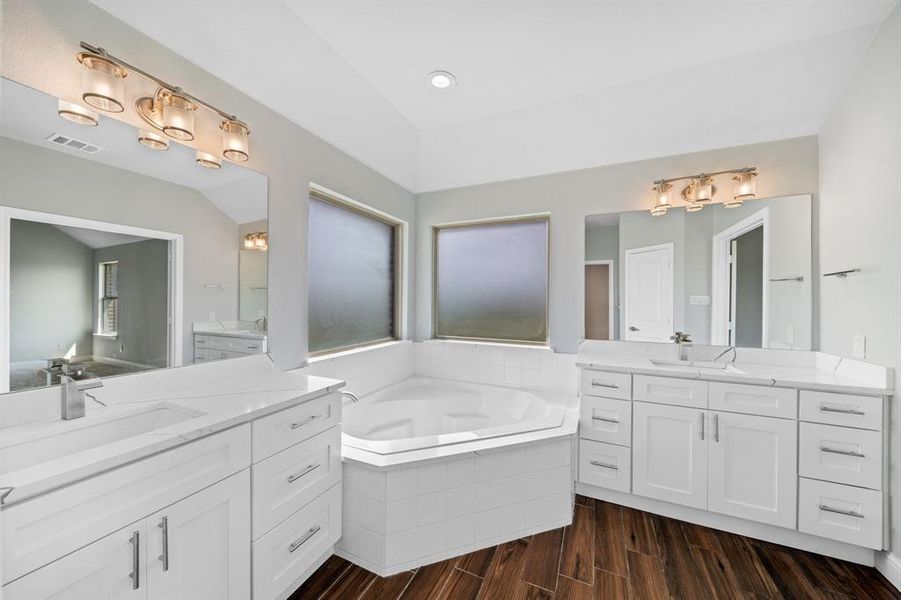 Bathroom with hardwood / wood-style flooring, dual bowl vanity, and a relaxing tiled tub