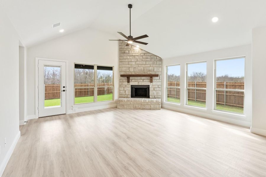 Open living room with vaulted ceiling, stone fireplace, ceiling fan, and light hardwood floors