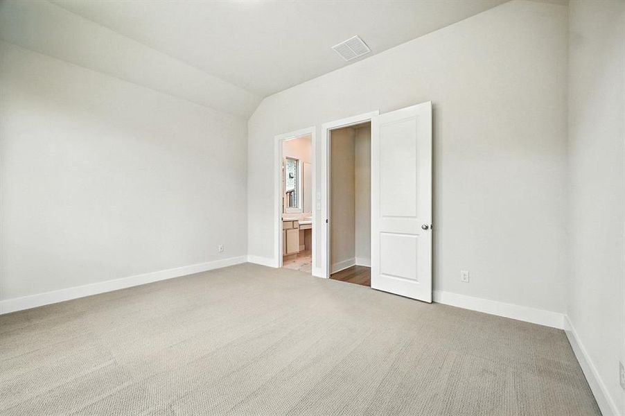 Unfurnished bedroom featuring light colored carpet, lofted ceiling, and connected bathroom Unfurnished bedroom featuring light colored carpet, lofted ceiling, and connected bathroom