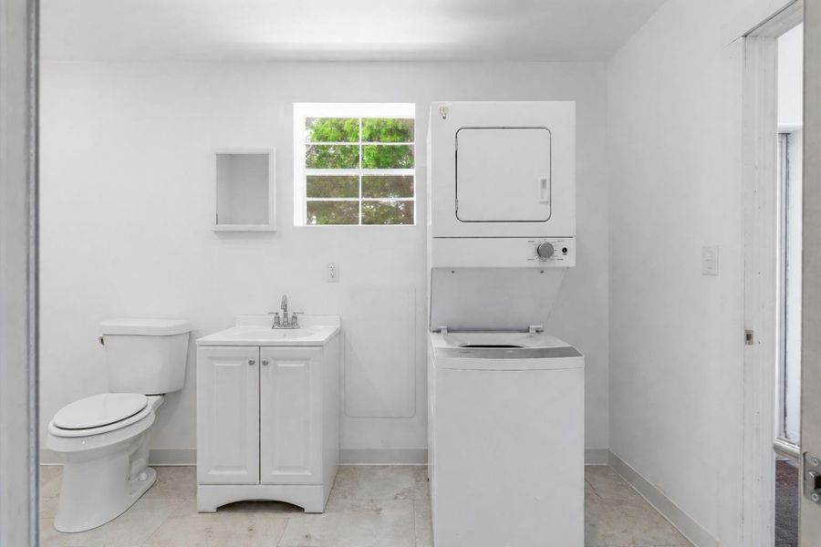 The utility room features a white stacked washer and dryer, a toilet, and a white vanity with a sink