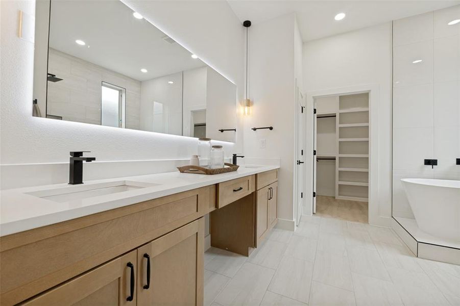 Bathroom featuring a double vanity with light wood-finish cabinetry, integrated sinks, and matte black hardware