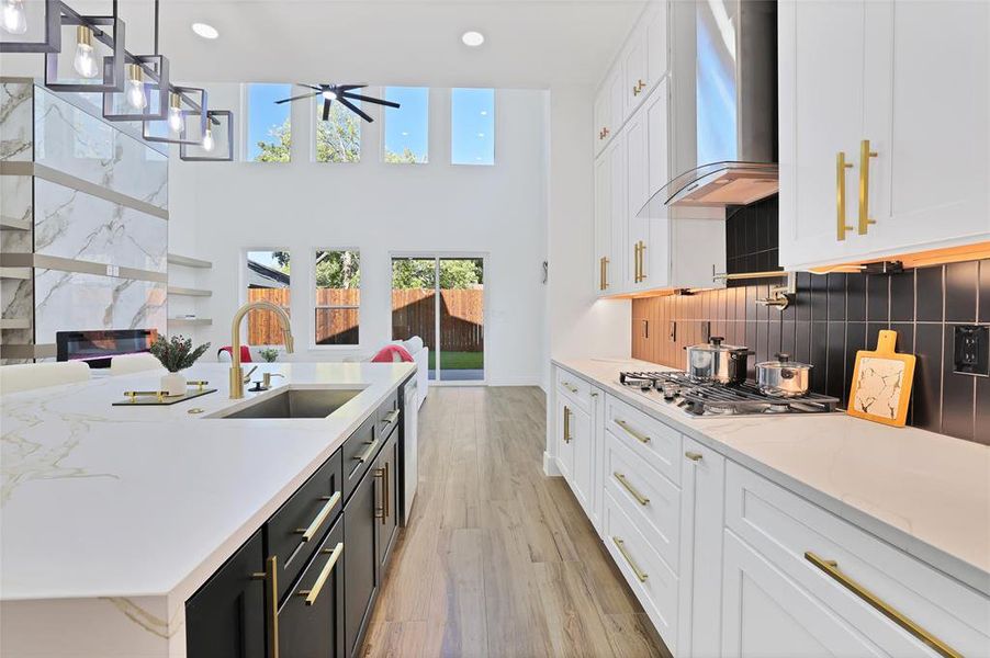 Kitchen with wall chimney exhaust hood, a sink, white cabinetry, plenty of natural light, and a high ceiling