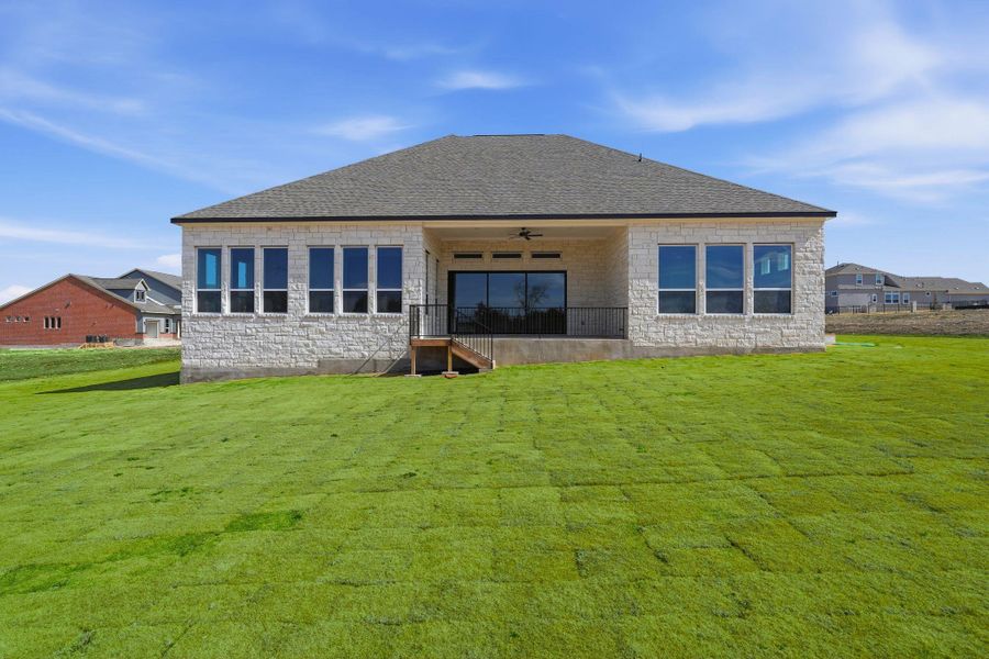 Rear view of property featuring stone siding, ceiling fan, a patio, a lawn, and roof with shingles