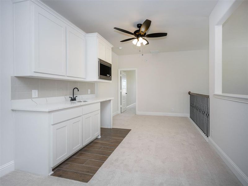 Kitchen with white cabinetry, light colored carpet, decorative backsplash, light stone counters, and ceiling fan Kitchen with white cabinetry, light colored carpet, decorative backsplash, light stone counters, and ceiling fan