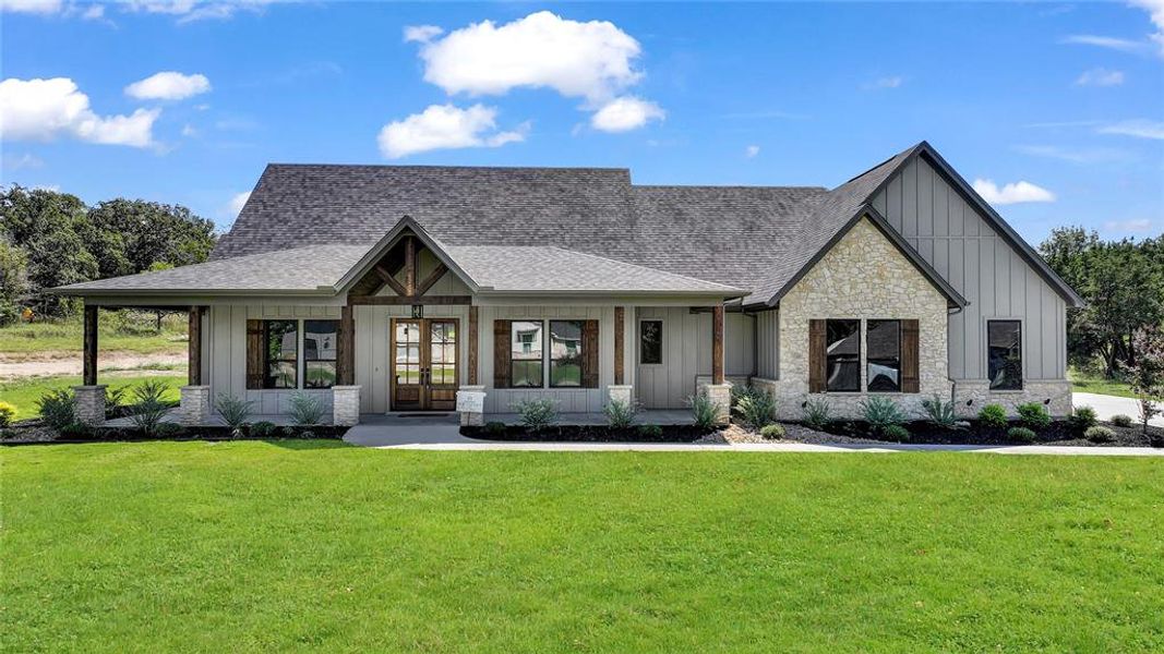 Modern inspired farmhouse with board and batten siding, covered porch, french doors, stone siding, and a front yard