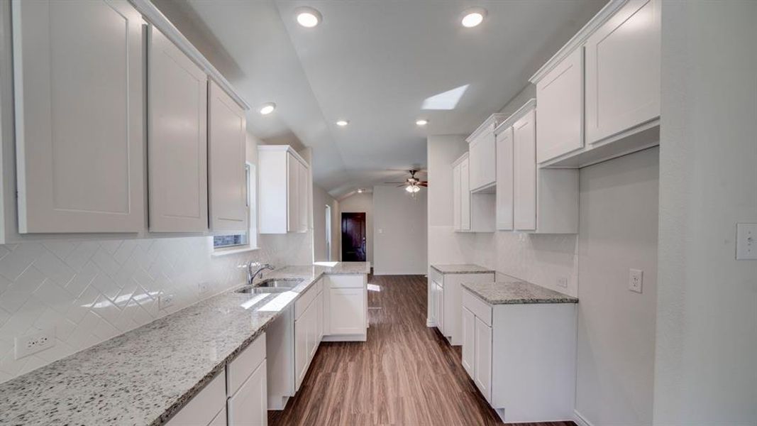Kitchen with lofted ceiling, white cabinets, light stone countertops, dark wood-style flooring, and a skylight