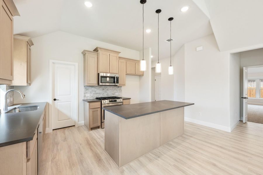 Kitchen with center island, light wood cabinets, stainless steel appliances, and pendant lights over dark countertops