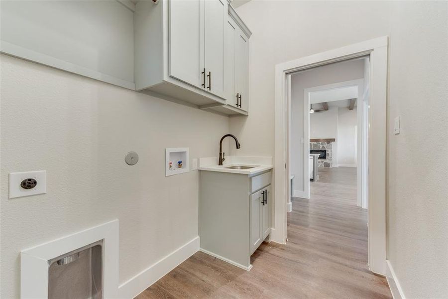 Laundry area with sink, washer hookup, cabinets, electric dryer hookup, and light hardwood / wood-style floors