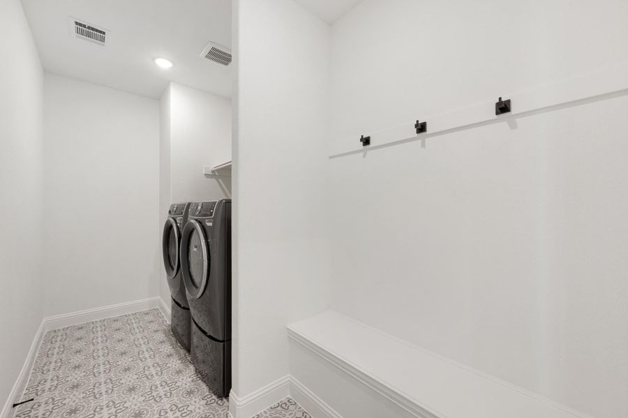 Laundry and mudroom area with front-load washer and dryer, built-in bench, wall hooks, and patterned tile floor Laundry and mudroom area with front-load washer and dryer, built-in bench, wall hooks, and patterned tile floor