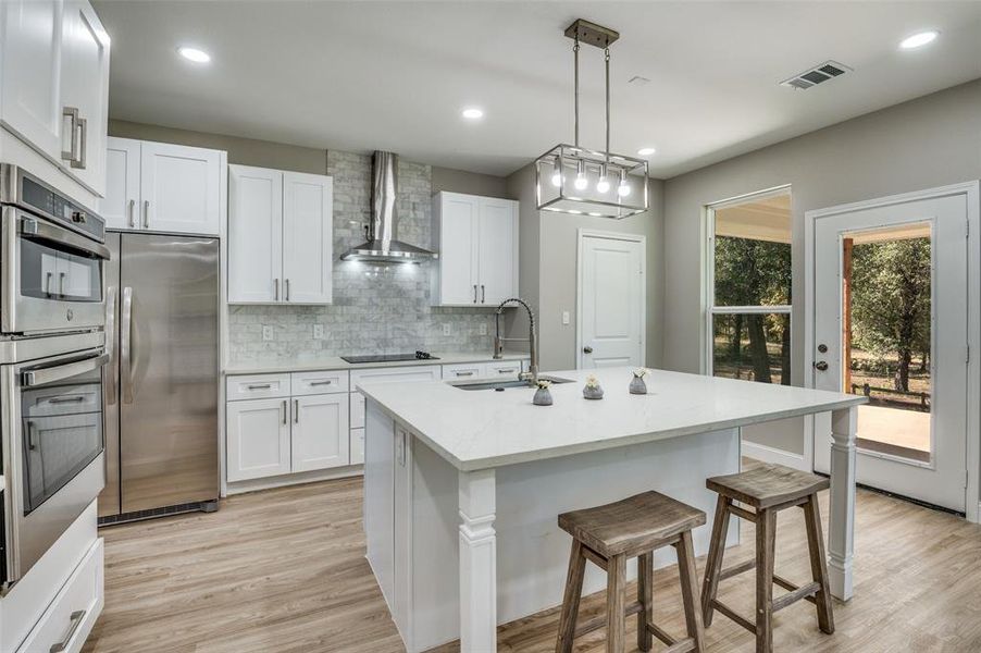 Kitchen featuring a kitchen bar, appliances with stainless steel finishes, hanging light fixtures, light wood-type flooring, and backsplash
