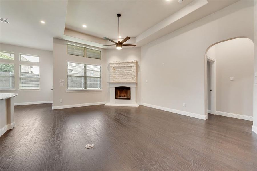 Unfurnished living room with a raised ceiling, a ceiling fan, a fireplace, arched walkways, and dark wood-style floors Unfurnished living room with a raised ceiling, a ceiling fan, a fireplace, arched walkways, and dark wood-style floors