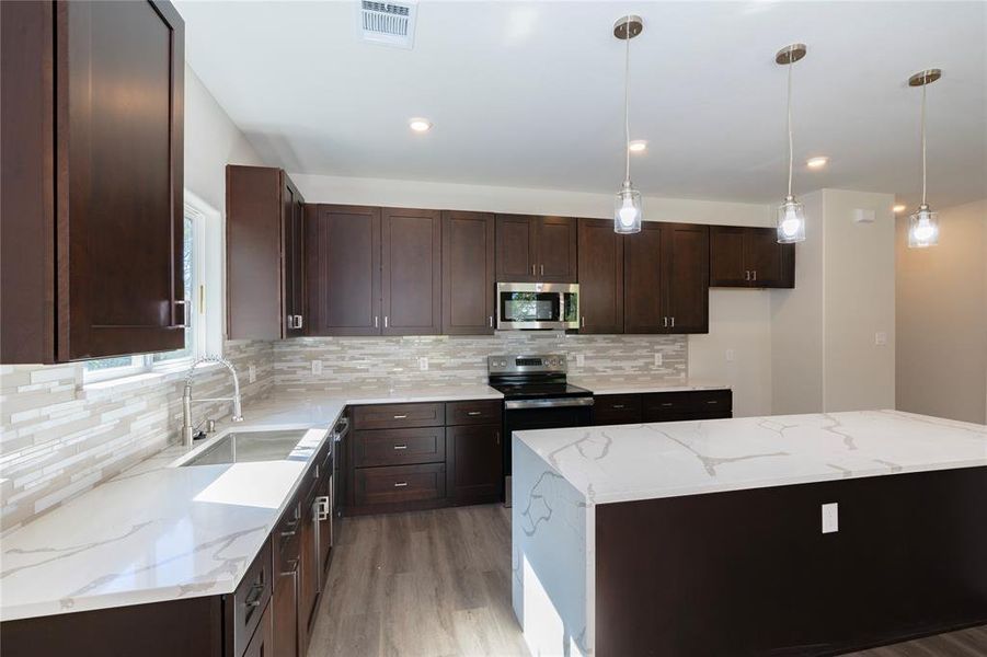 Kitchen with light stone counters, appliances with stainless steel finishes, hanging light fixtures, sink, and a center island