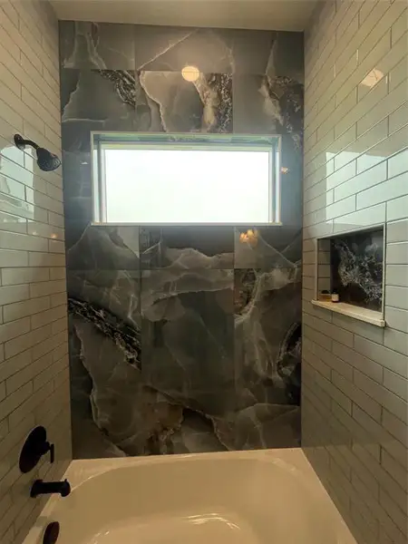 Bathtub and shower combination featuring large format marble-look tile, subway tile surround, matte black fixtures, and a recessed niche