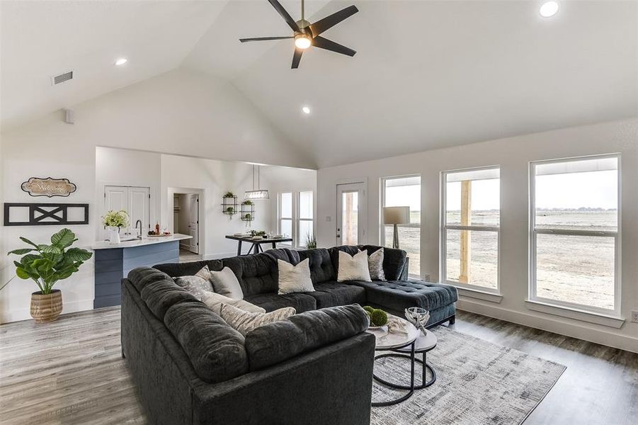 Living room featuring a ceiling fan, visible vents, high vaulted ceiling, and wood finished floors