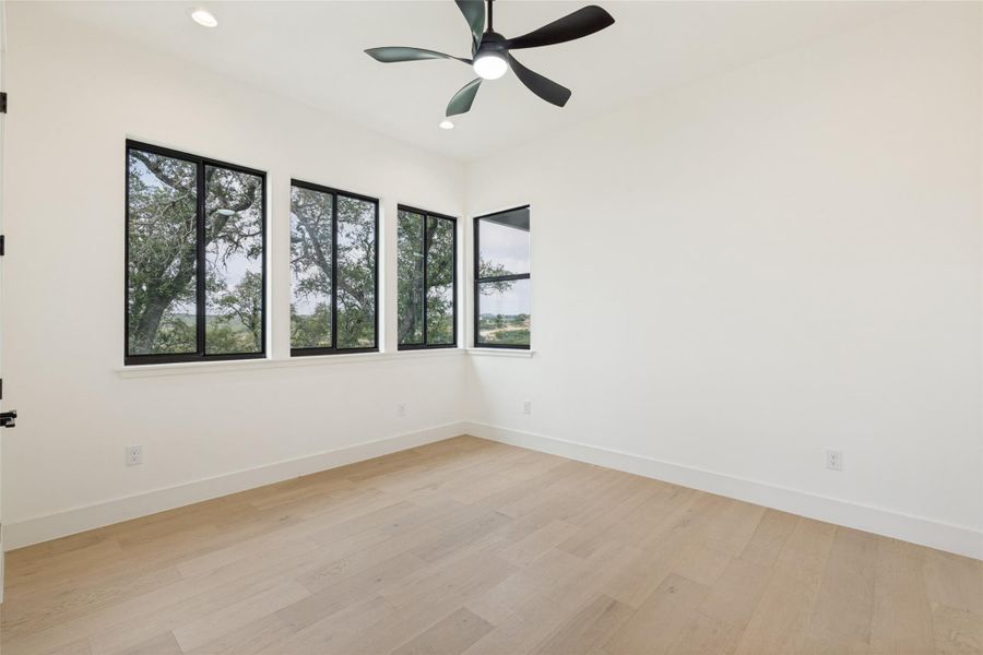 Bright windows offer verdant views, complementing light wood flooring and a modern ceiling fan.