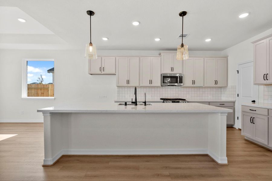 This light and bright kitchen features a large quartz island, custom stained cabinets, a large sink overlooking your family room, recessed lighting, and beautiful backsplash.