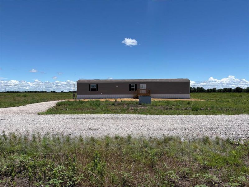 Single-story residence featuring neutral-toned siding, a gravel driveway, and a partially covered foundation Single-story residence featuring neutral-toned siding, a gravel driveway, and a partially covered foundation