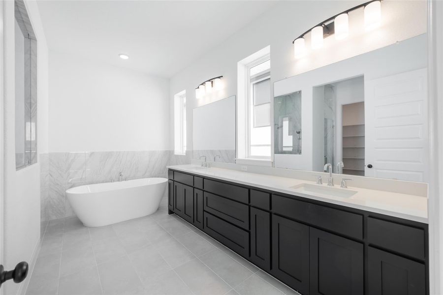 Primary Full bathroom featuring double vanity, a wainscoted wall, a freestanding tub, tile walls, and light tile patterned floors