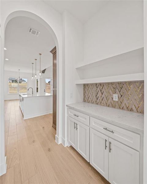 Built-in cabinetry with stone countertop, decorative tile backsplash, and light wood-finish flooring