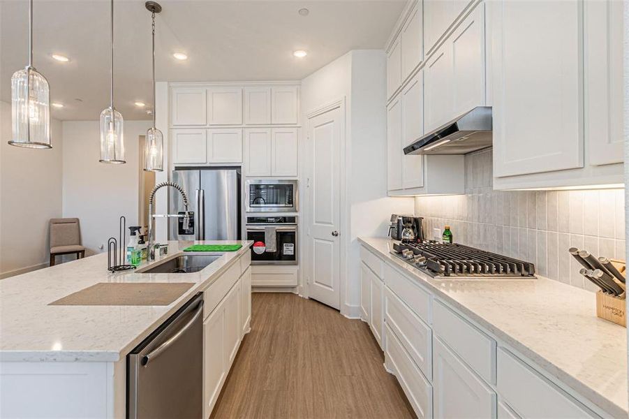 Kitchen with white cabinets, light stone countertops, hanging light fixtures, light wood-style floors, and recessed lighting