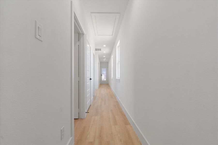 Hall featuring baseboards, visible vents, attic access, and light wood-style floors