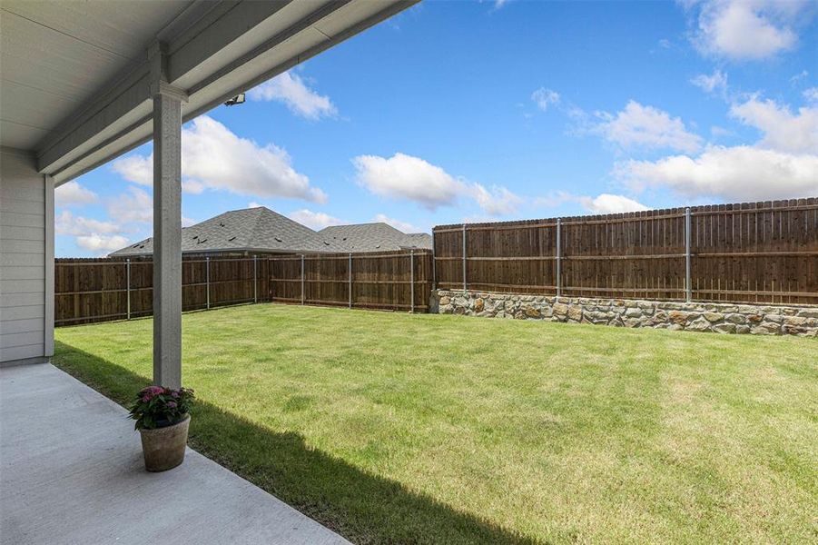 Spacious backyard featuring a manicured lawn, full privacy fencing, and a stone retaining wall Spacious backyard featuring a manicured lawn, full privacy fencing, and a stone retaining wall