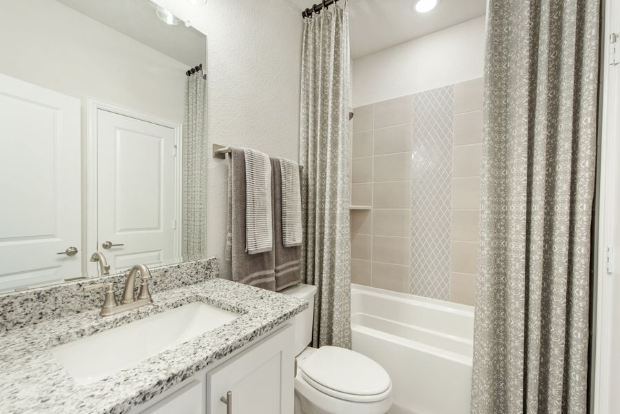 Bathroom with granite countertop vanity, toilet, and tiled tub-shower combo with gray curtain