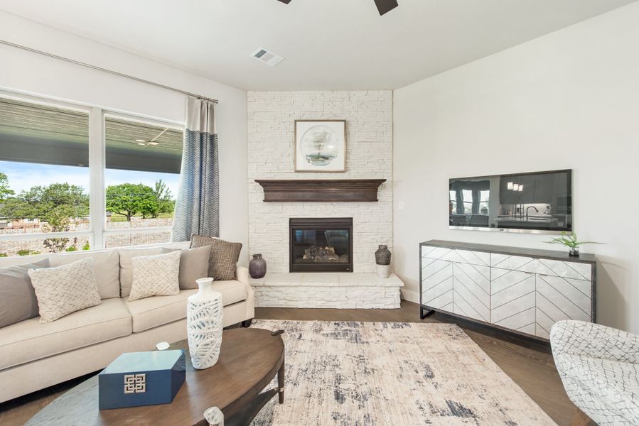 Living room with white stone fireplace, beige sofa, dark wood coffee table, and large window with outdoor view