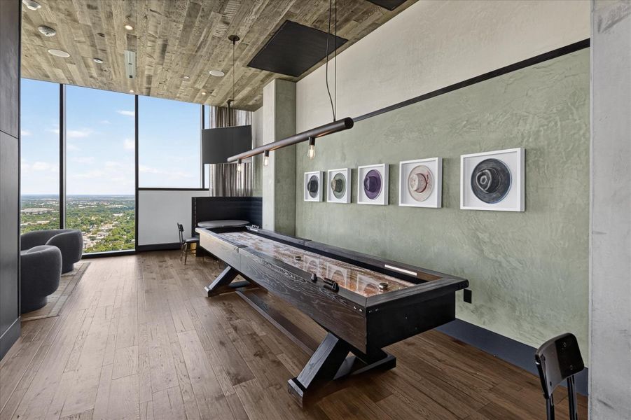 An inviting recreation room with expansive city views and a chic shuffleboard table, perfect for entertaining.