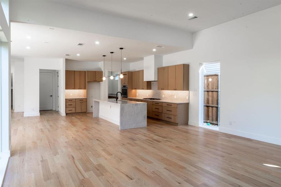 Kitchen with sink, decorative backsplash, light wood-type flooring, an island with sink, and decorative light fixtures