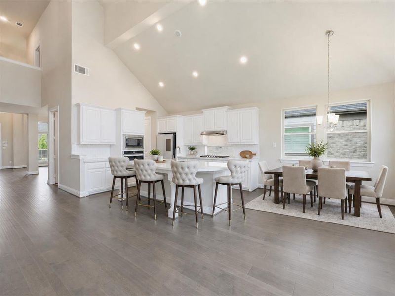 Expansive kitchen and dining area featuring vaulted ceilings with recessed lighting, wood-finish flooring, a kitchen island with seating, white cabinetry, and stainless steel appliances