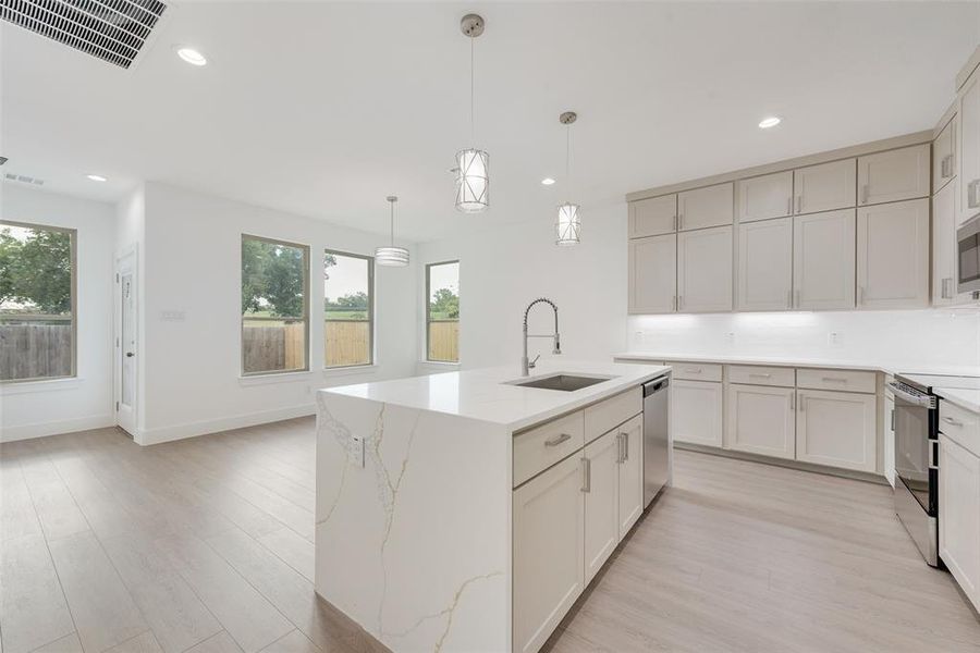 Kitchen with light wood-style floors, recessed lighting, decorative light fixtures, a center island with sink, and light stone countertops Kitchen with light wood-style floors, recessed lighting, decorative light fixtures, a center island with sink, and light stone countertops